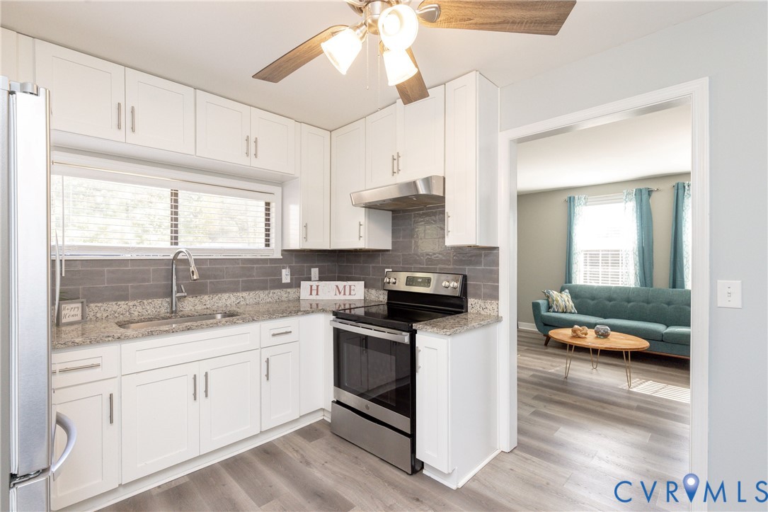 Kitchen featuring white shaker-style cabinetry, stone-finish countertops, stainless steel appliances, a grey subway tile backsplash, and wood-finish flooring