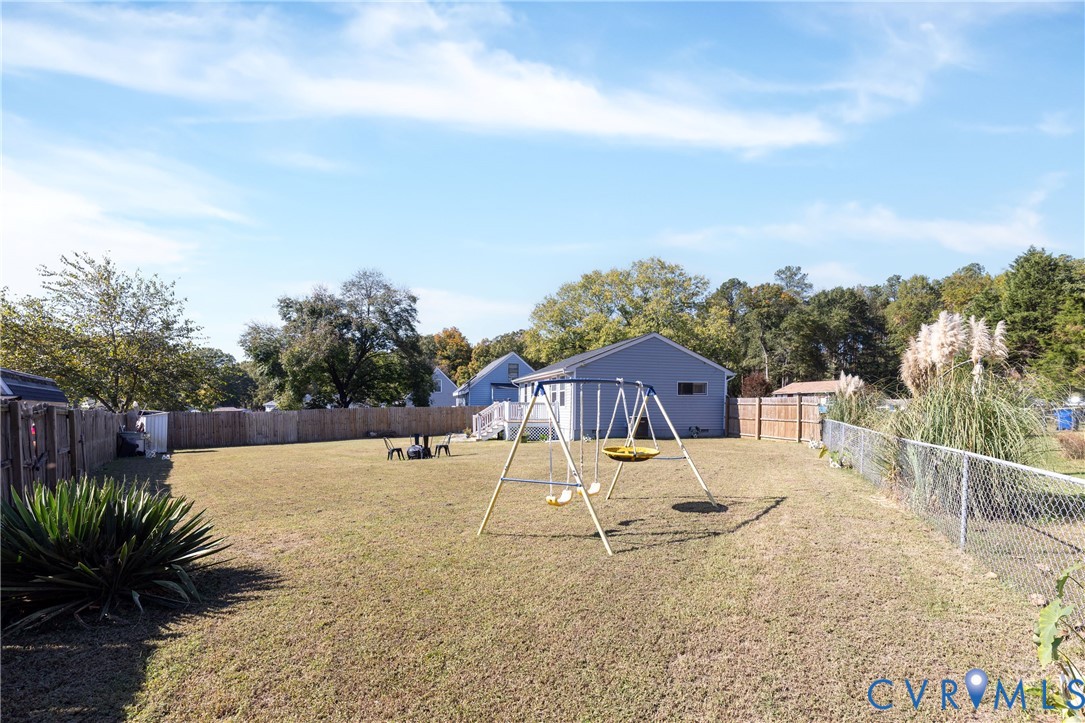 Expansive backyard featuring a large grass lawn, perimeter wood fencing, and metal chain-link sections
