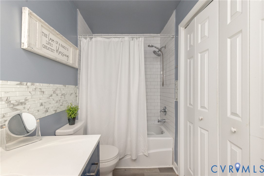 Bathroom featuring a tub-shower combination with white subway tile surround, decorative stone-finish tile accent, dual-panel bifold closet doors, and wood-finish flooring