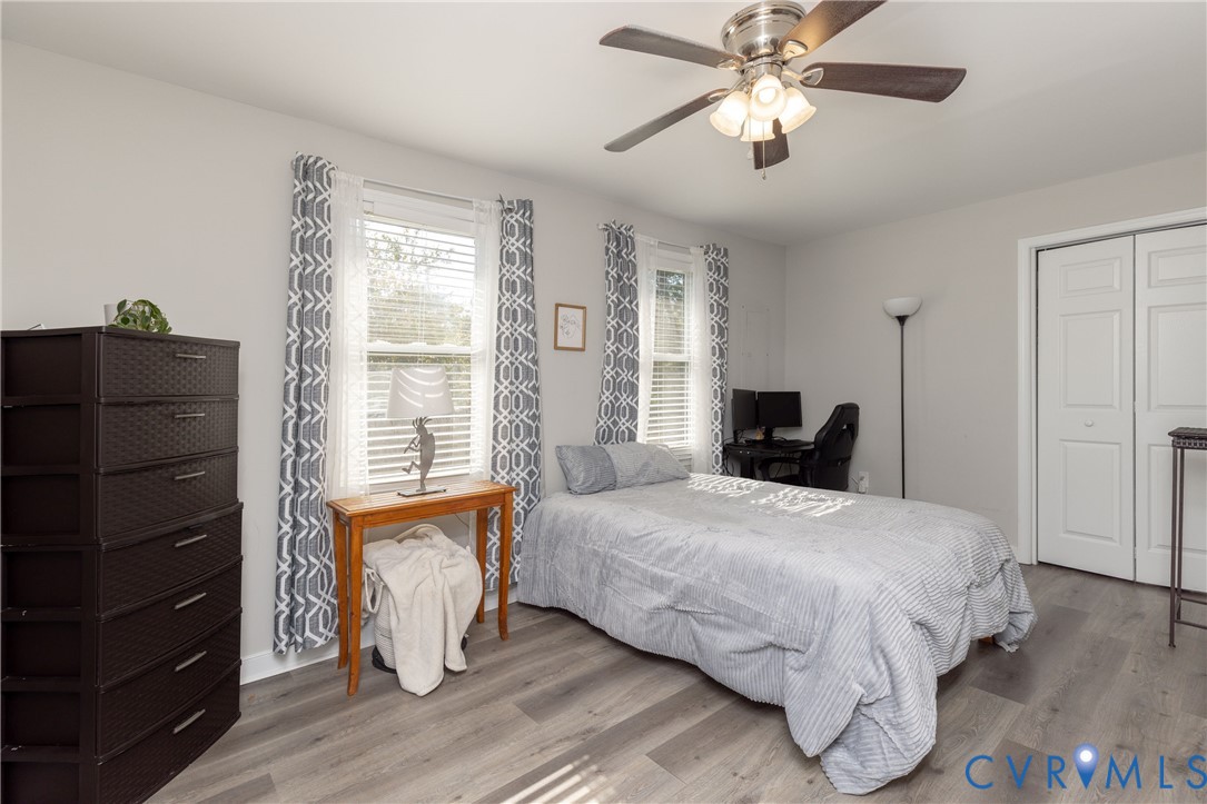 Wood-finish flooring, ceiling fan with integrated lighting, dual windows with blinds, and double-panel closet doors