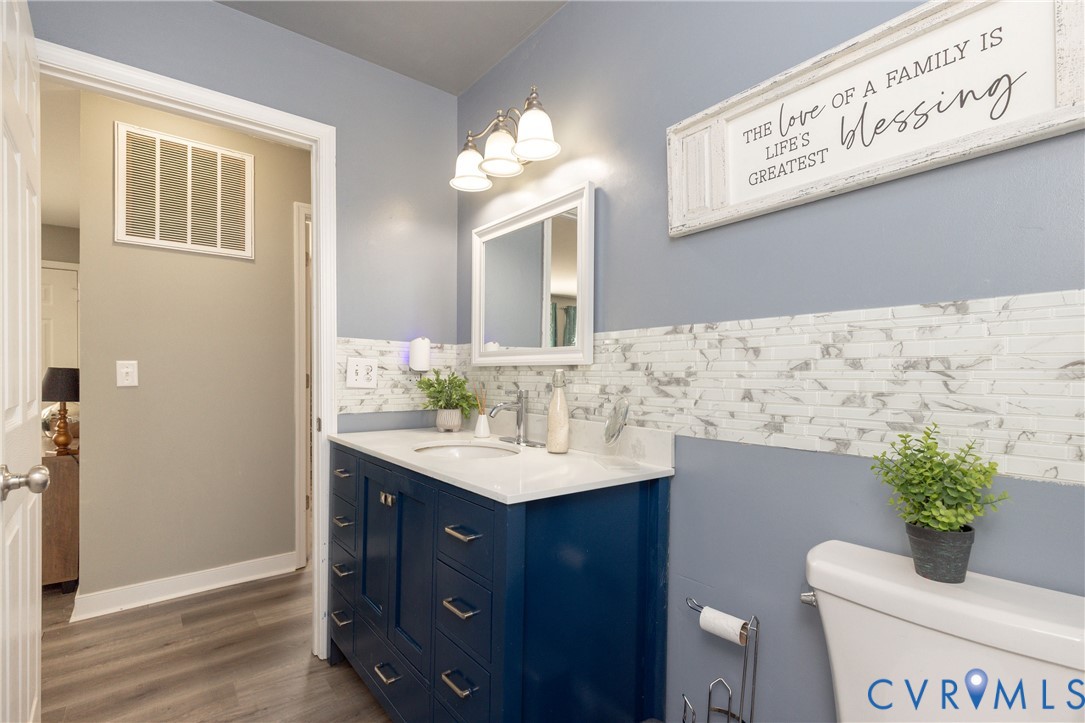 Blue vanity cabinet with white countertop, integrated sink, decorative tile backsplash, three-light wall fixture, and wood-finish flooring