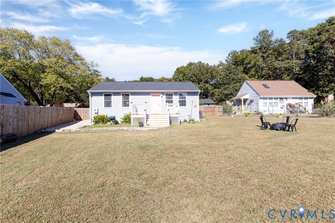 Single-story residence featuring light-colored horizontal siding, a pitched asphalt shingle roof, a raised entry deck with stairs, and an expansive fenced backyard