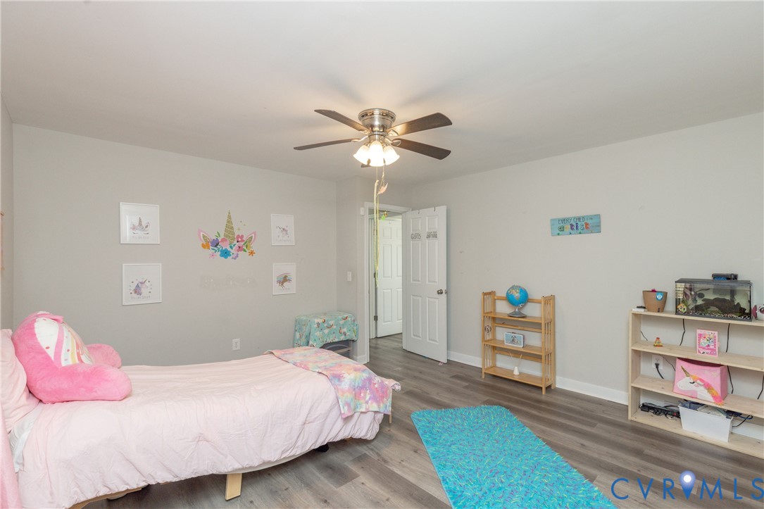 Neutral-toned interior featuring wood-finish flooring, a multi-blade ceiling fan with integrated lighting, and a paneled interior door