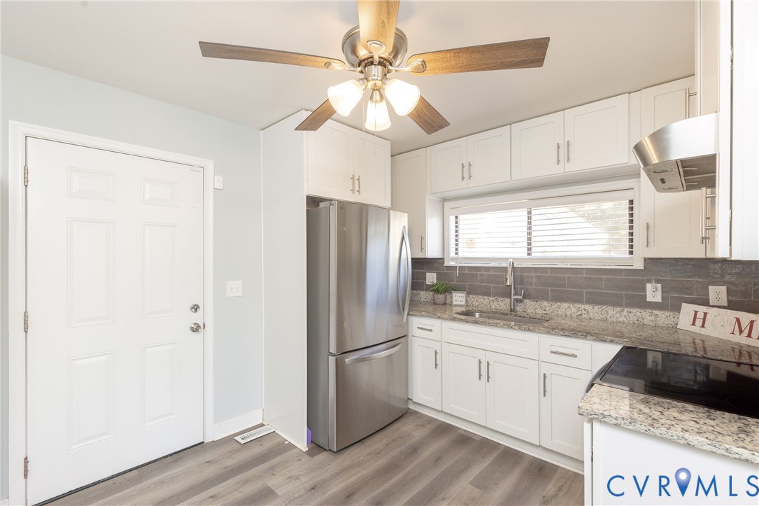 Kitchen featuring white cabinetry, stone-finish countertops, grey subway tile backsplash, stainless steel appliances, and wood-finish flooring
