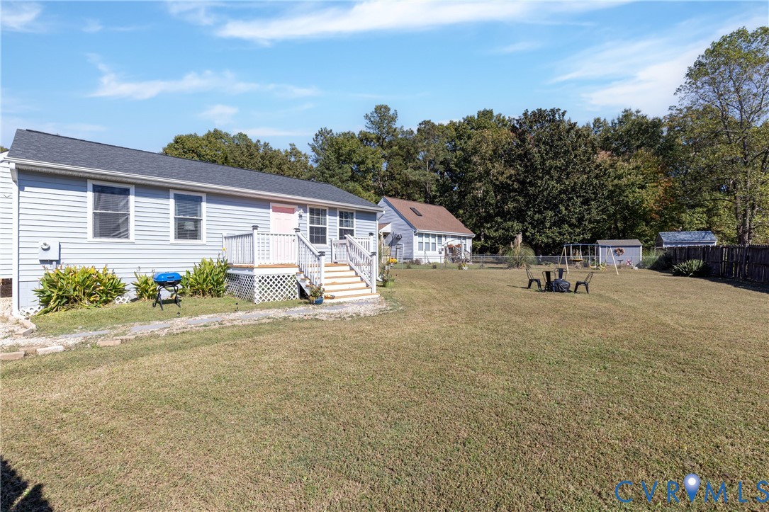 Large backyard featuring a grass lawn, privacy fencing, a storage shed, and a raised exterior deck with railing