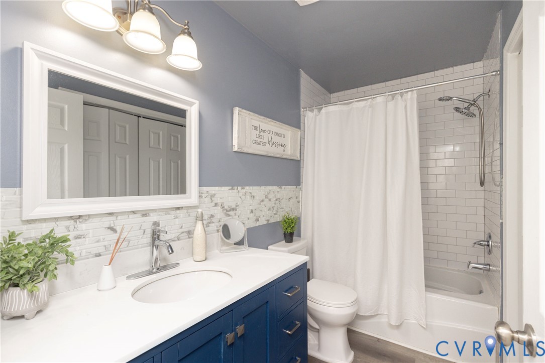 Bathroom featuring a vanity with white countertop and integrated sink, subway-tiled shower surround, three-light wall fixture, framed mirror, and chrome finish hardware