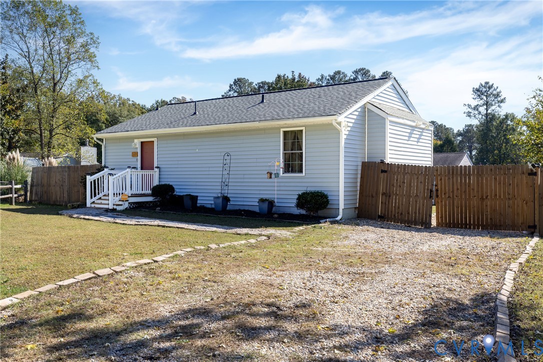 Light grey vinyl-sided exterior featuring an asphalt shingle roof, gravel driveway, wood-picket fencing, and a front entry porch with white railings