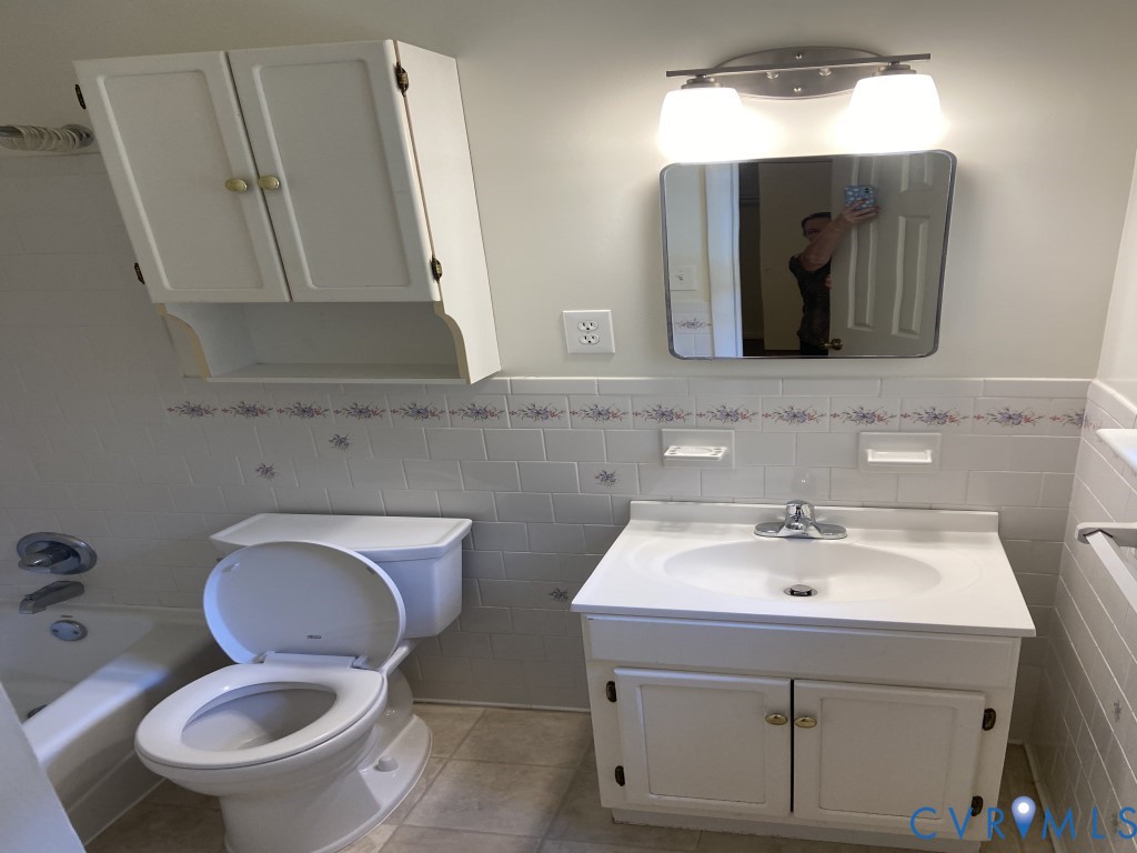 White vanity with an integrated countertop, wall-mounted storage cabinet, subway-tiled backsplash with decorative accents, and dual-light vanity fixture