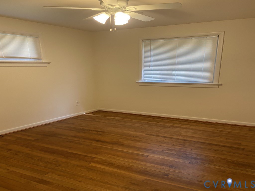 Room featuring wood-finish flooring, neutral wall paint, two windows with horizontal blinds, and a ceiling-mounted light fixture