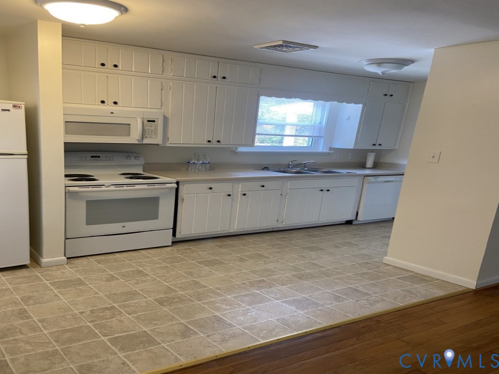 Kitchen featuring white cabinetry, solid-surface countertops, dual-basin sink, integrated white appliances, and tiled flooring