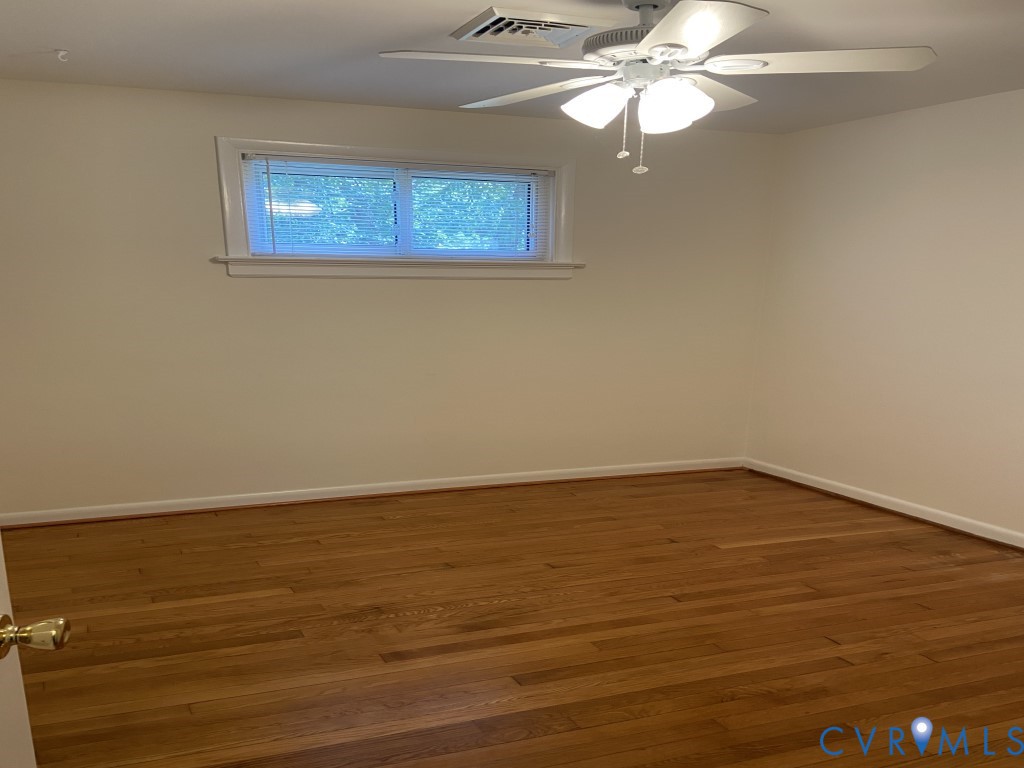 Room interior featuring wood-finish flooring, a ceiling fan with integrated light fixture, and a single-hung window with casing