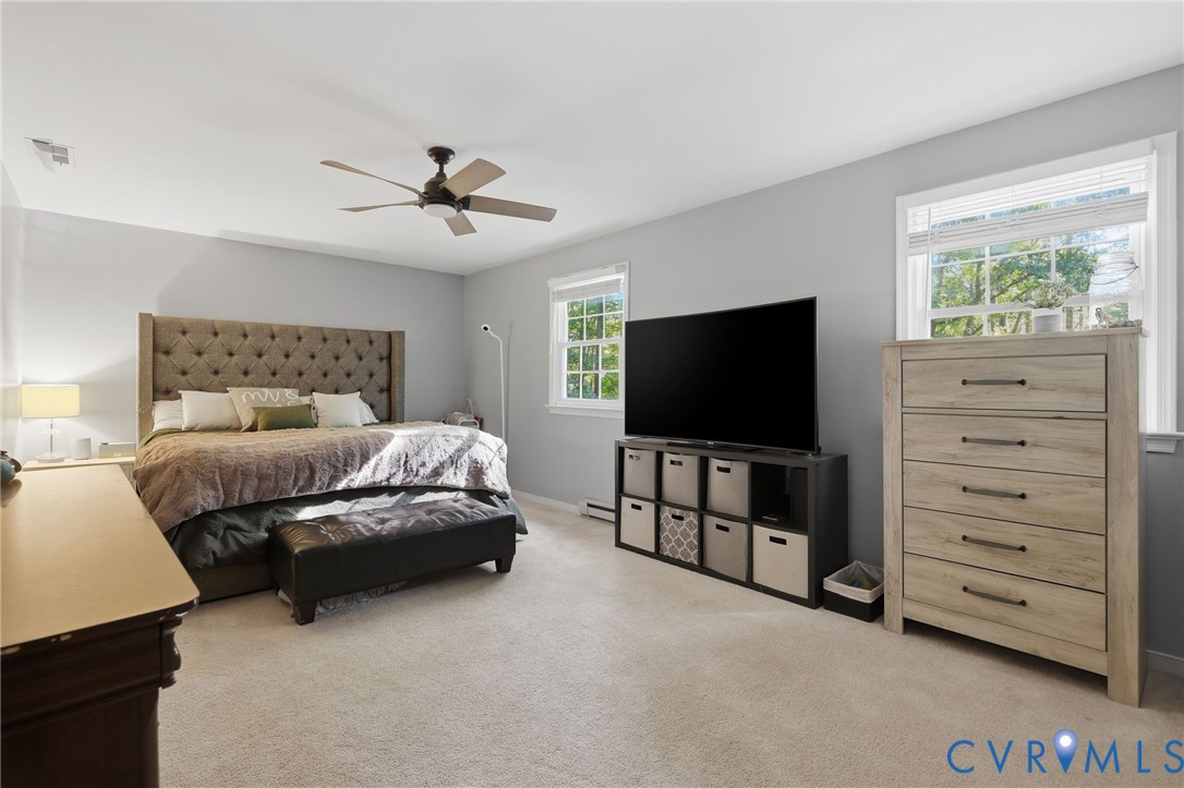 Spacious primary bedroom on second floor room featuring neutral carpeting, a ceiling fan, and multiple windows