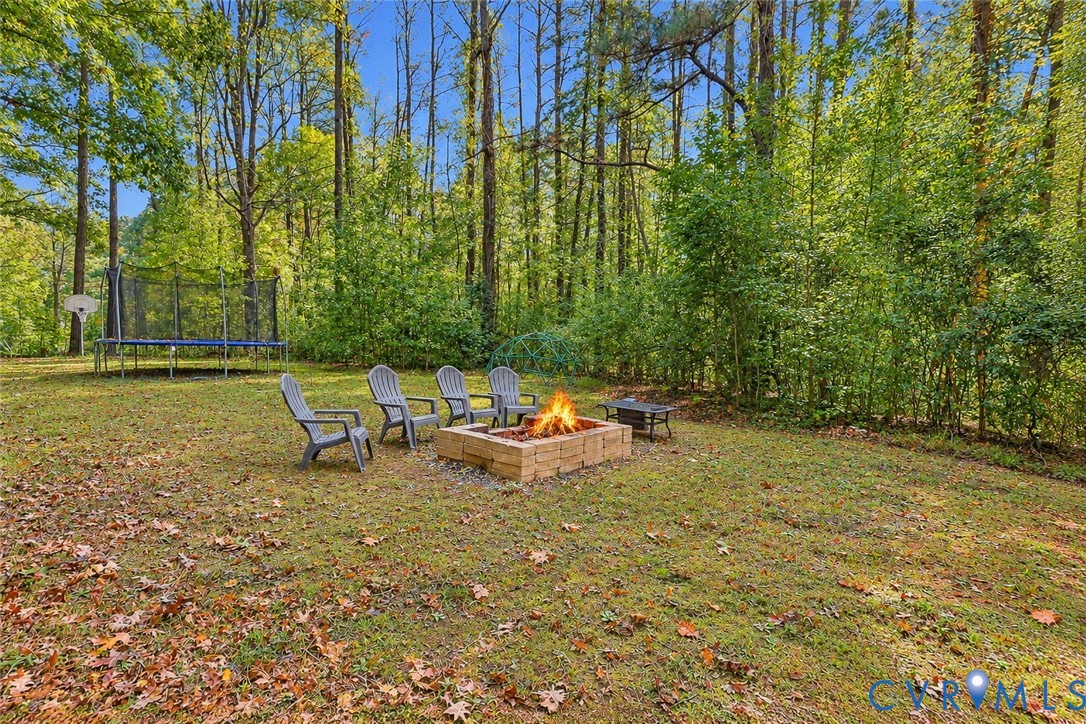 More front yard featuring a stone fire pit and a backdrop of dense mature trees