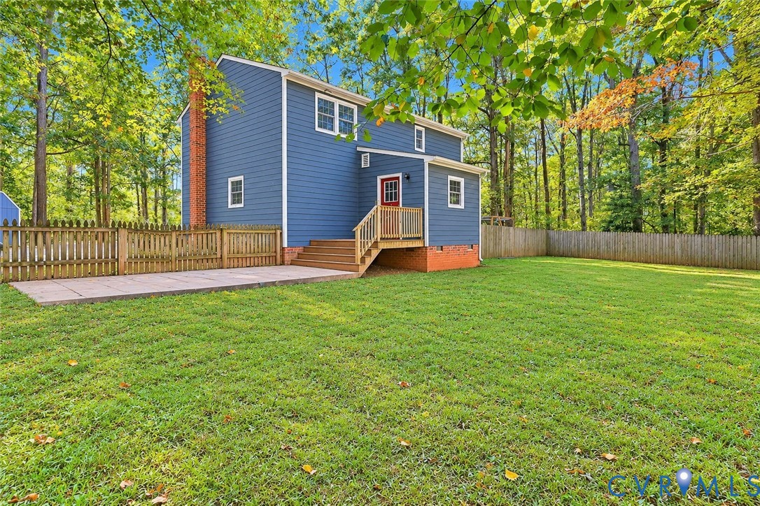 Rear exterior featuring blue horizontal siding,  a wood deck with stairs, a concrete patio, and perimeter wood fencing *Photo digitally enhanced; grass and select personal items removed*