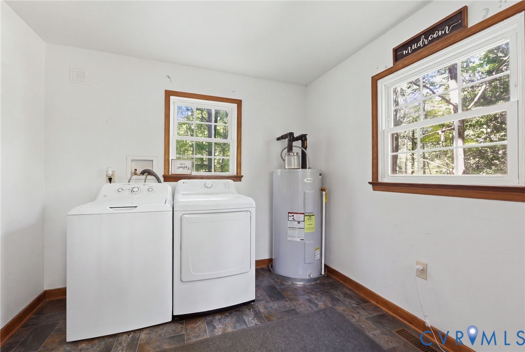 Utility area featuring dual windows with wood trim,and water heater *Select personal items digitally removed using AI*