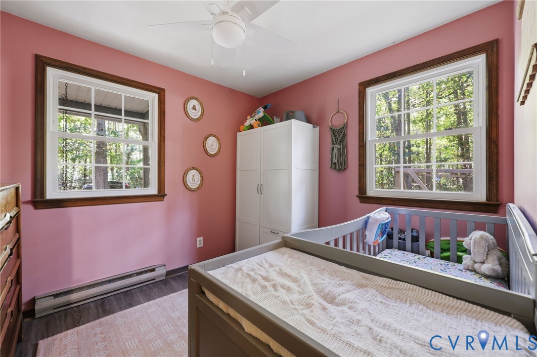 Bedroom #2 option downstairs featuring two windows with wood trim, wood-finish flooring, and a ceiling fan