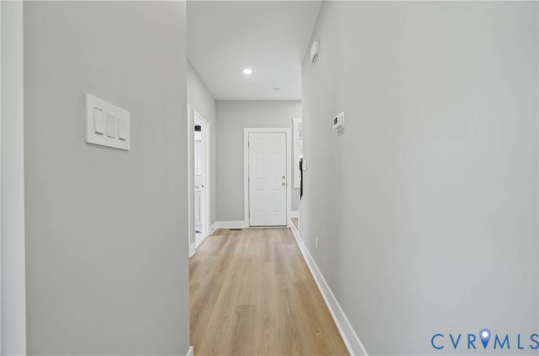 Hallway featuring wood-finish flooring, neutral wall tones, recessed lighting, and a six-panel door