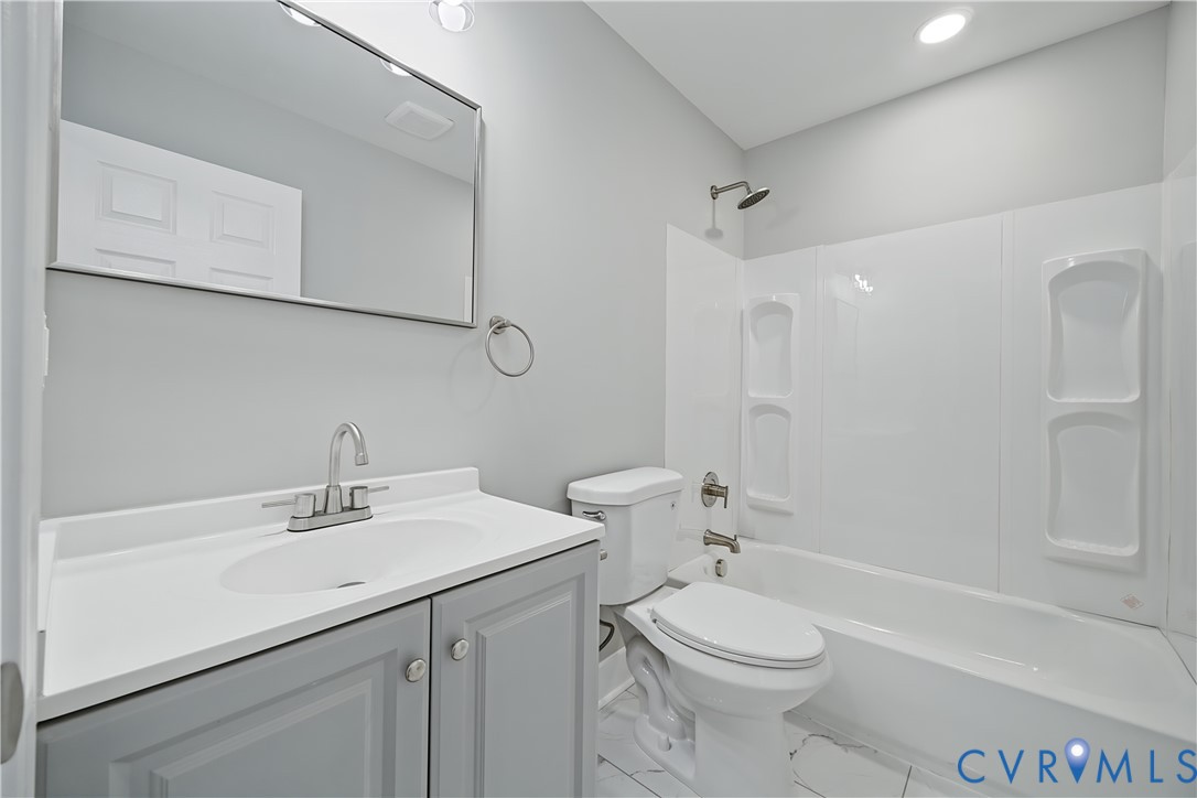 Bathroom featuring a vanity with a solid-surface countertop, integrated basin, and brushed-nickel faucet, complemented by a combination tub and shower with a white acrylic surround and built-in shelving