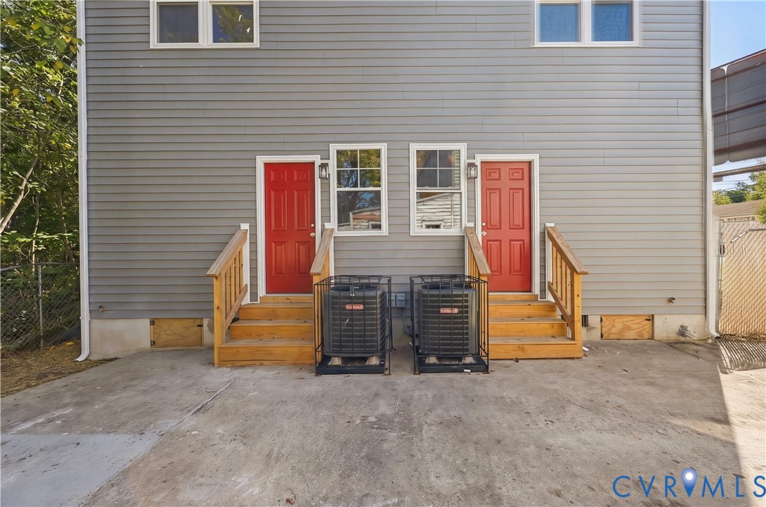 Horizontal lap siding exterior featuring two elevated wood-finished staircases, dual red entry doors, and dedicated exterior heating and cooling units