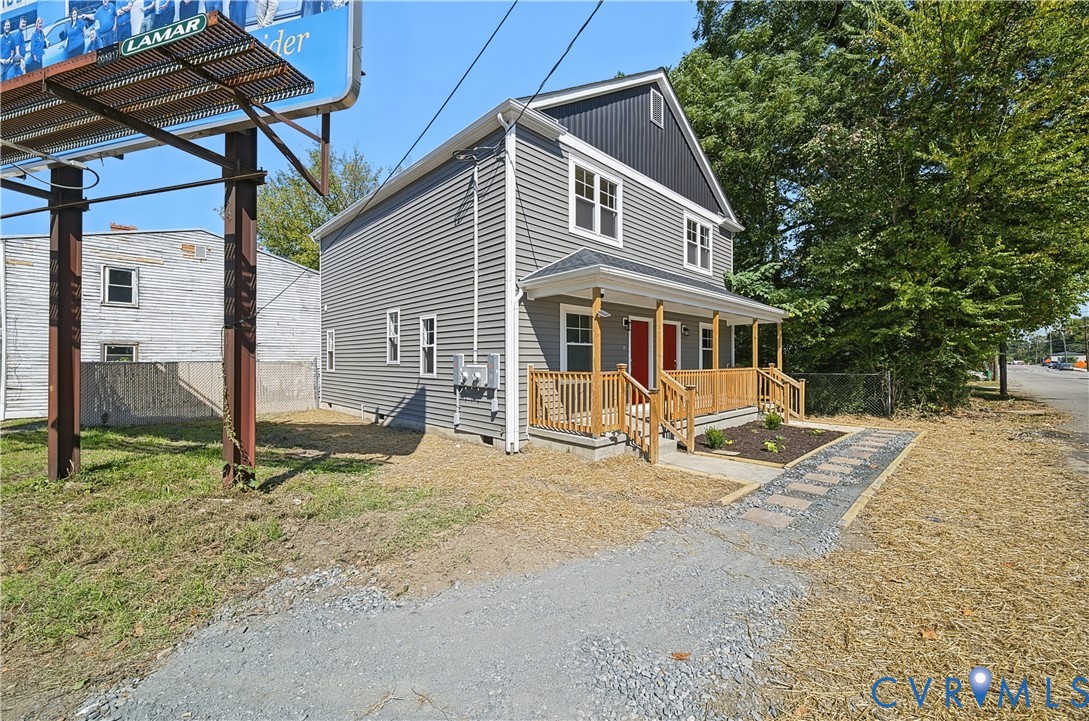 Two-story residence featuring gray horizontal siding, black vertical board-and-batten gable detailing, an expansive wooden front porch, and a stone paver walkway
