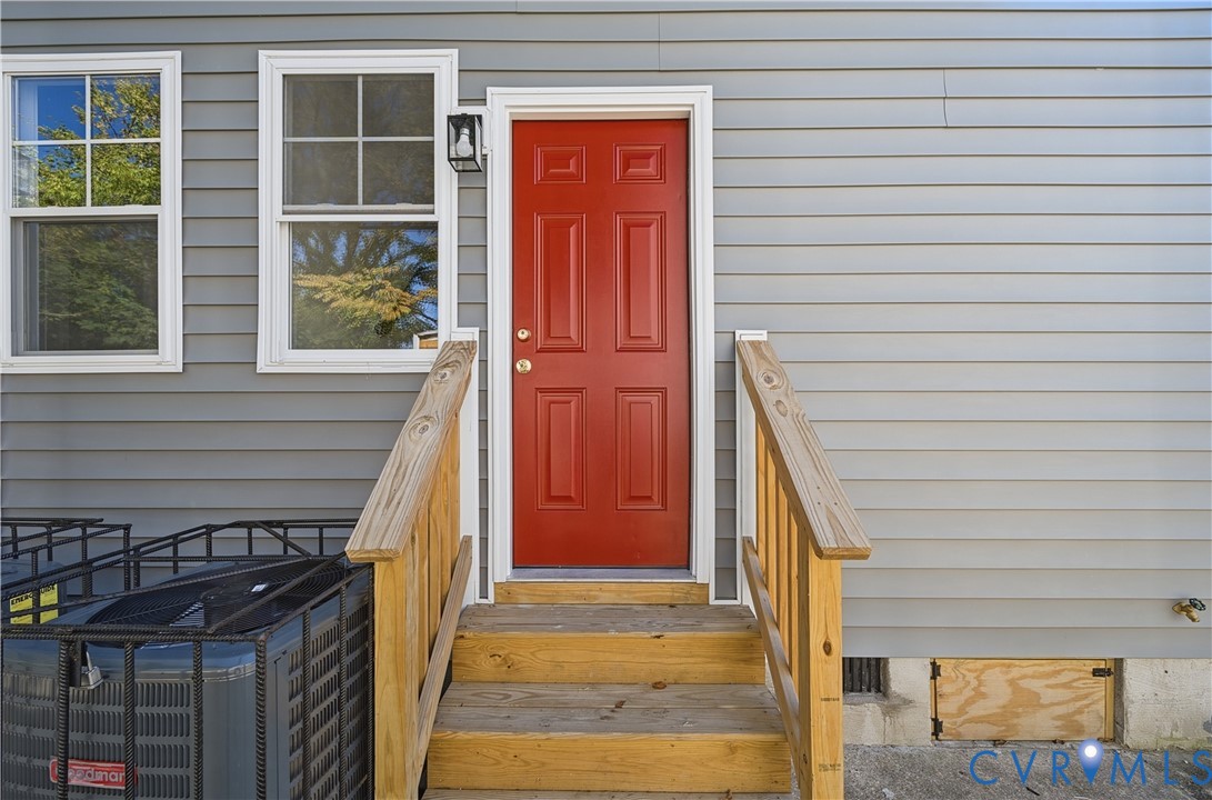 Exterior featuring horizontal vinyl siding, a paneled red entry door, multi-pane windows, and wooden stairs with matching handrails