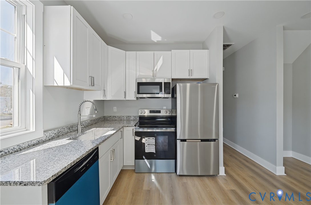 Kitchen featuring white shaker-style cabinetry, stone-finish countertops, stainless steel appliances, and wood-finish flooring