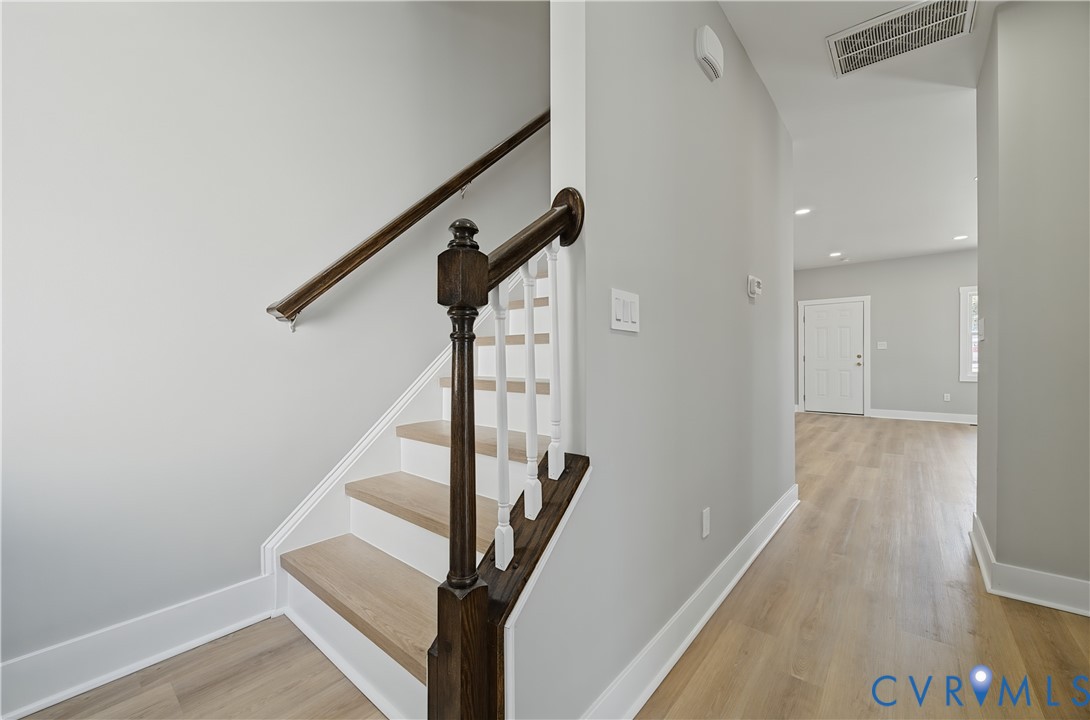 Staircase featuring wood-finish treads, a dark-stained handrail, and white vertical balusters complemented by wood-finish flooring throughout the hallway