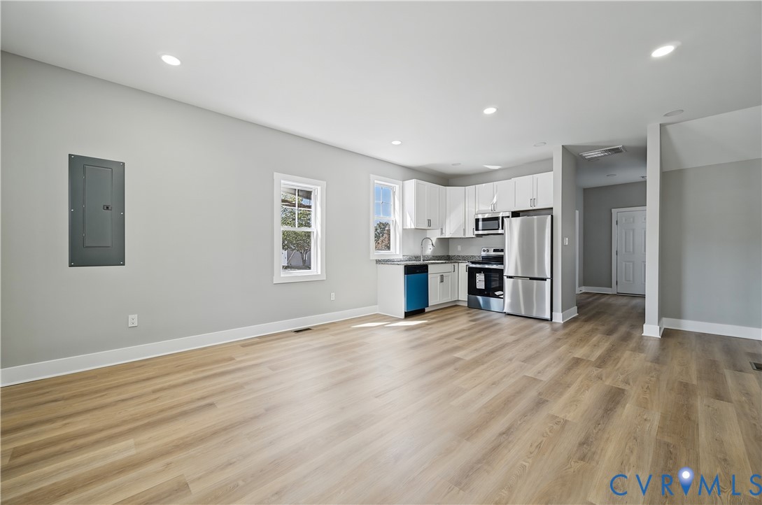 Kitchen area featuring white shaker-style cabinetry, stainless steel appliances, dark stone-finish countertops, recessed lighting, and wood-finish flooring