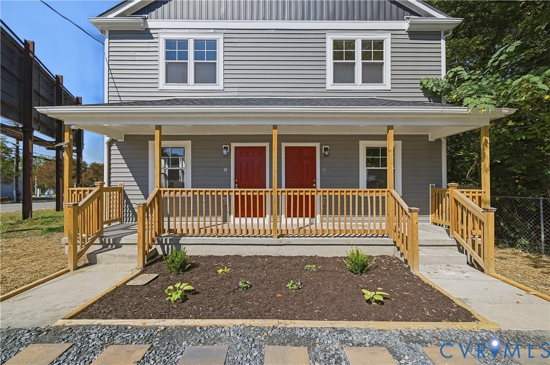 Exterior featuring grey horizontal siding, a covered front porch with wood railings, two red entry doors, and a landscaped front garden bed