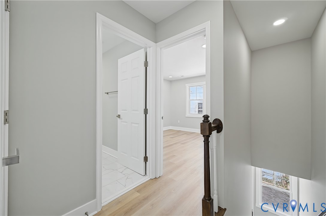 Hallway featuring wood-finish flooring, recessed lighting, multi-panel doors, and a staircase with a stained-wood baluster