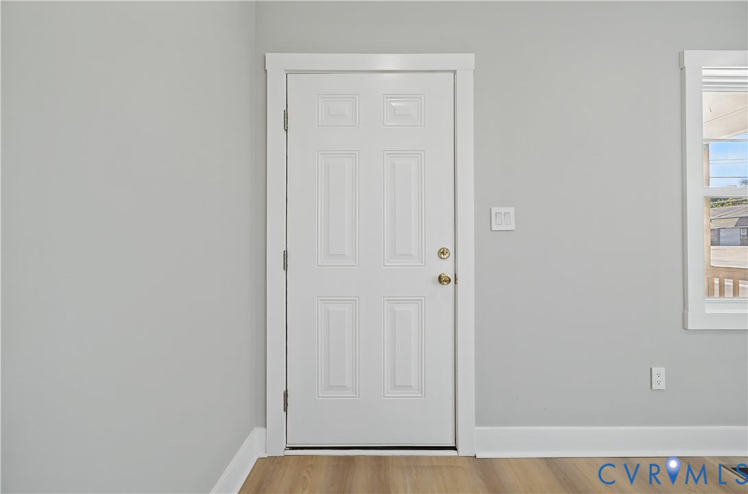 Six-panel interior door with brass-tone hardware, wood-finish flooring, and white window casing
