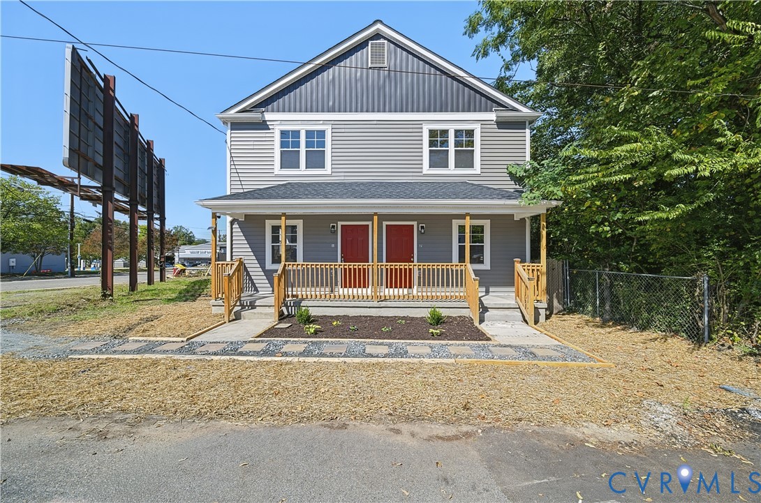 Two-story structure featuring grey vinyl siding, dual red front entry doors, a covered porch with wooden railing, and architectural shingle roofing