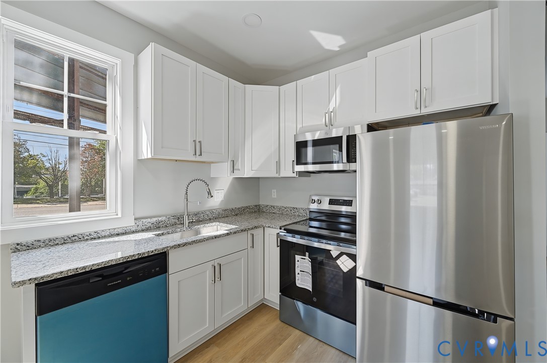 Kitchen featuring white shaker-style cabinetry, stone-finish countertops, stainless steel appliances, and wood-finish flooring