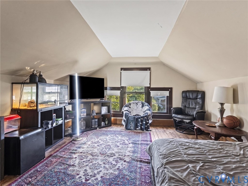 Bedroom featuring vaulted ceilings, wood flooring, and multi-pane windows with dark-stained wood trim