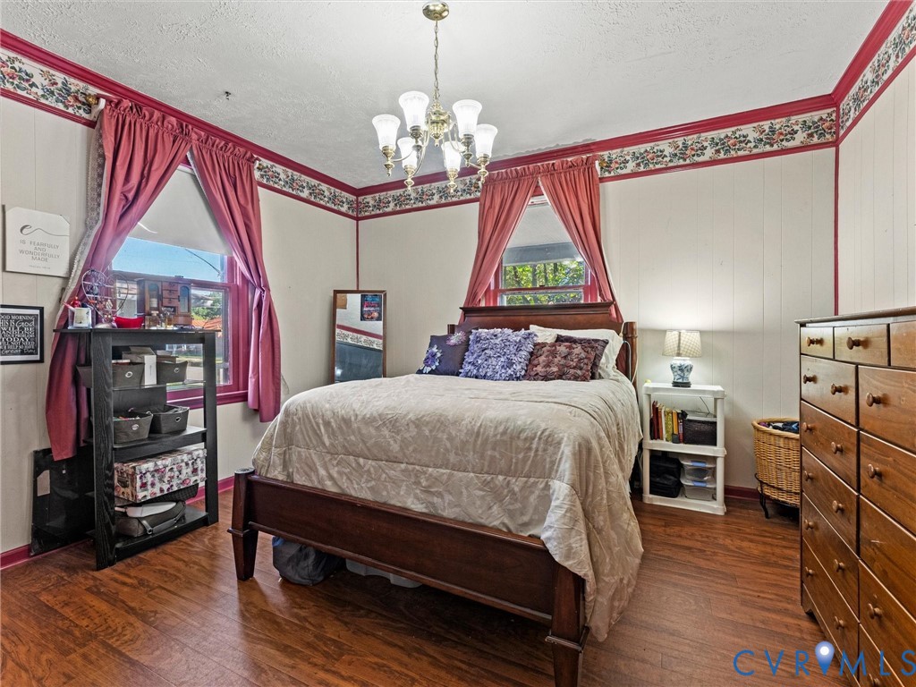 Bedroom with wood-finish flooring, multi-light chandelier, and paneled walls with decorative border trim