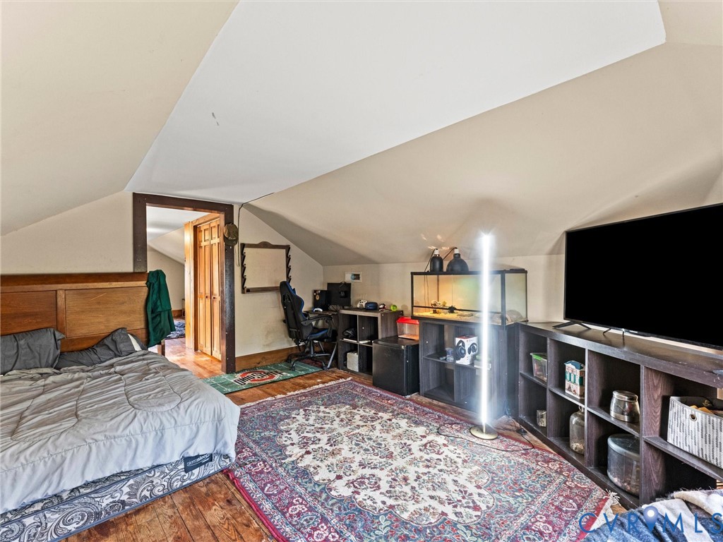 Bedroom featuring vaulted ceilings, dark-stained wood trim, and wood flooring