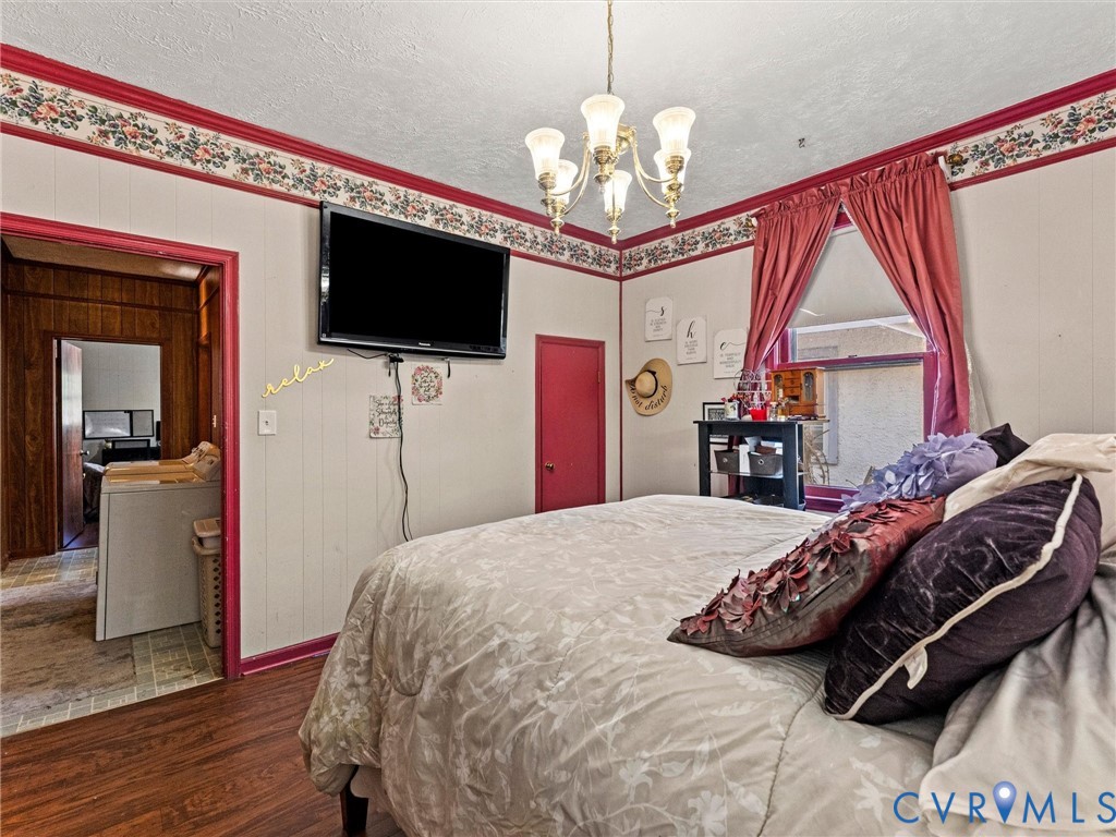 Bedroom with wood-finish flooring, multi-arm chandelier, and floral wallpaper border