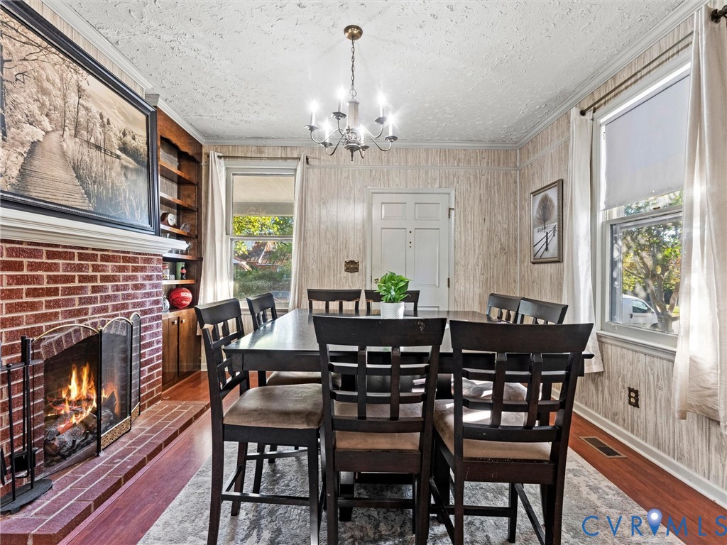 Red brick fireplace with a wood mantel, built-in shelving, wood-finish flooring, and a multi-arm chandelier. Flame is AI generated. Fireplace is not currently hooked to fuel source.