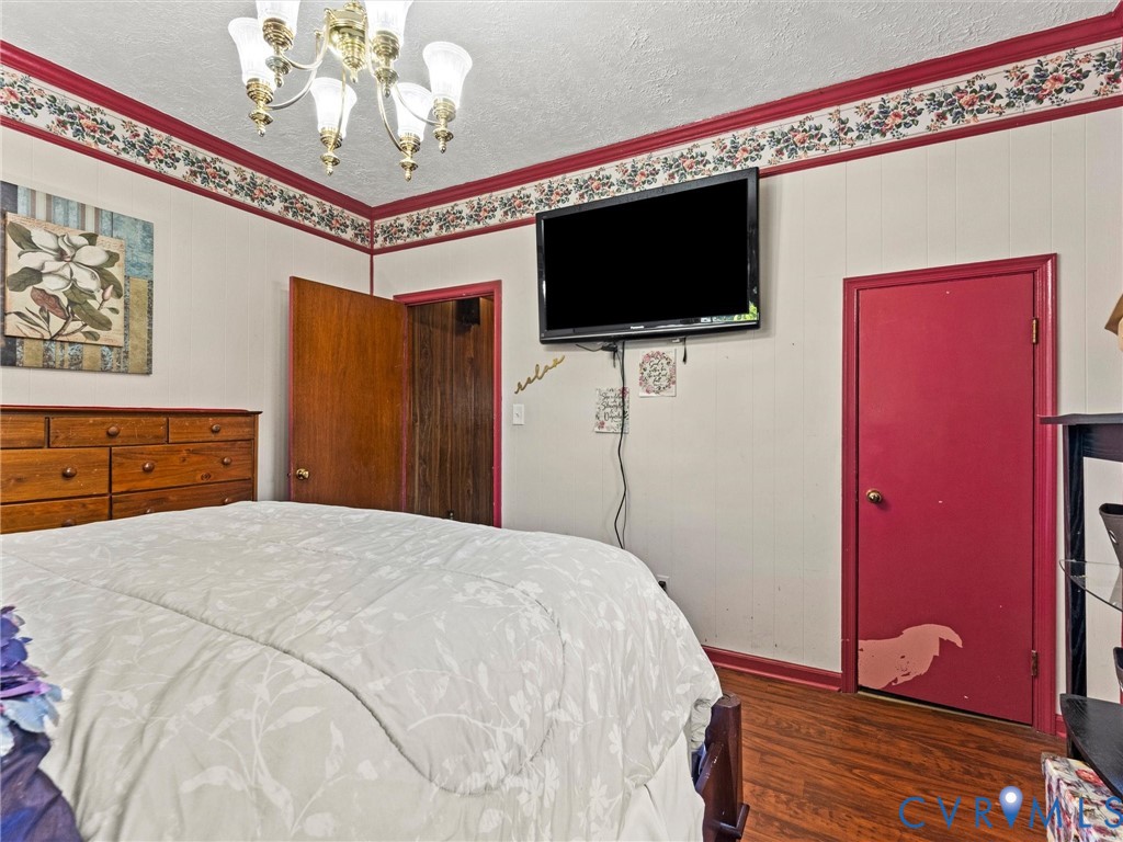 Bedroom featuring wood-finish flooring, decorative floral wallpaper border, and a classic multi-arm chandelier