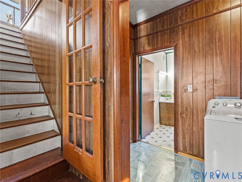 Wood-paneled walls, French door with glass panes, interior staircase with wood treads, and patterned vinyl flooring