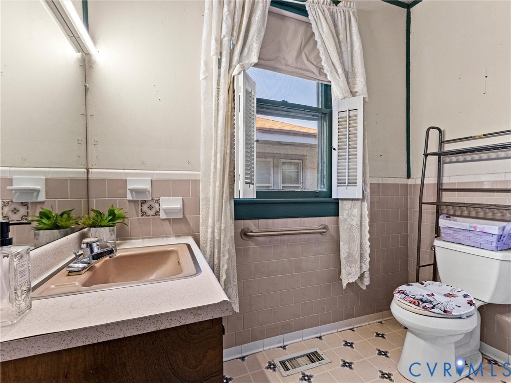 Bathroom featuring a vanity with an integrated sink, wall-mounted horizontal grab bar, ceramic wall tile wainscoting, and patterned vinyl tile
