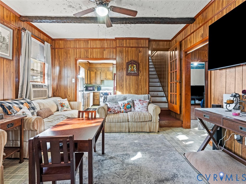 Living area featuring wood-paneled walls, exposed ceiling beams, and a mounted ceiling fan