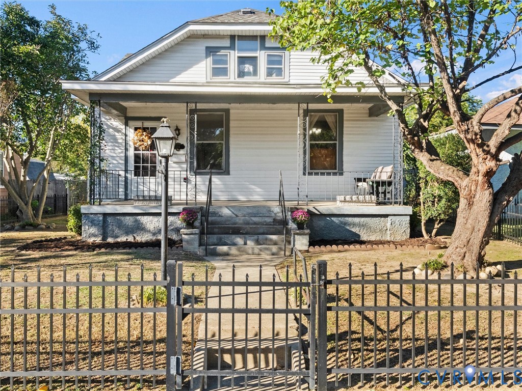 Bungalow residence featuring a covered front porch, horizontal siding, a concrete pathway, and an ornamental metal perimeter fence Bungalow residence featuring a covered front porch, horizontal siding, a concrete pathway, and an ornamental metal perimeter fence