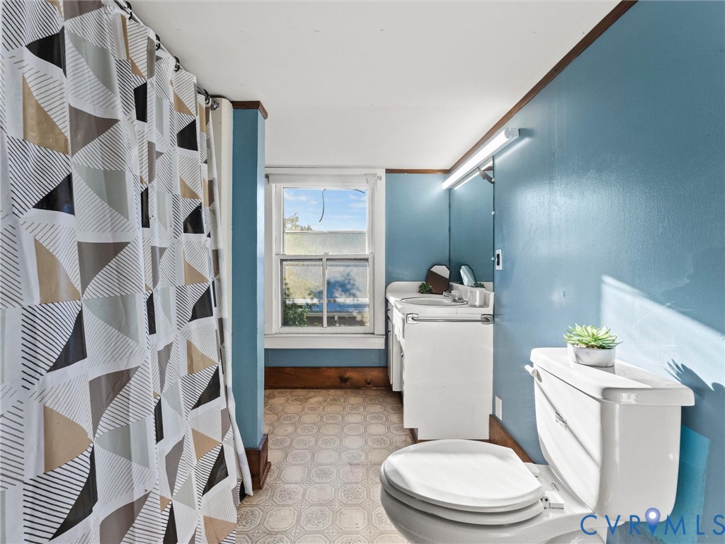 Bathroom featuring a white vanity cabinet with an integrated sink, wall-mounted vanity lighting, a large mirror, a multi-pane window, and patterned resilient flooring