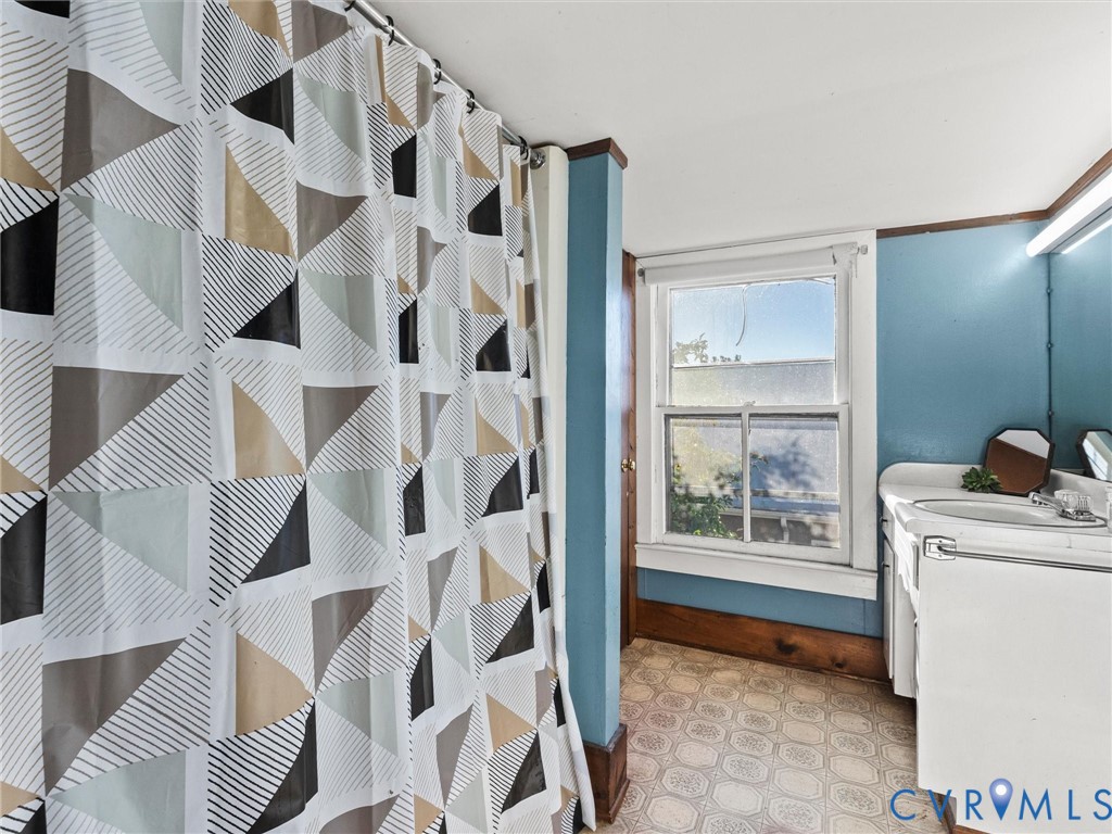 Bathroom featuring a white vanity cabinet, tub/shower combo, patterned sheet vinyl flooring, a single-hung window with wood trim
