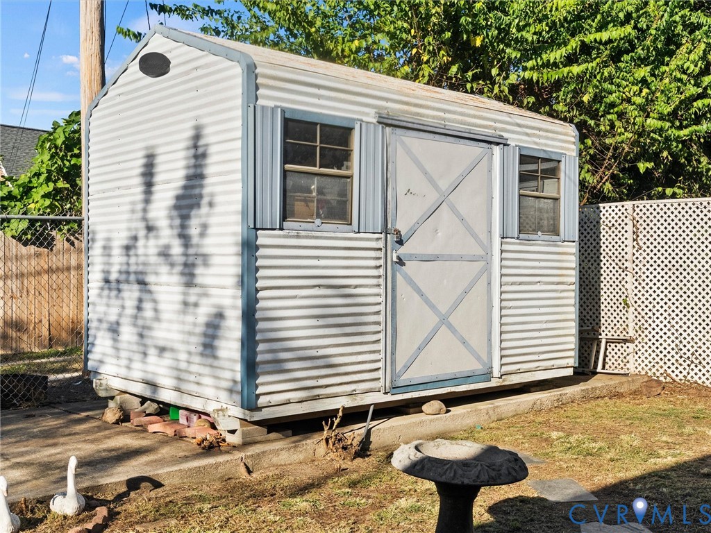 Storage shed featuring corrugated metal siding, two multi-pane windows, and a reinforced door, set upon a concrete foundation