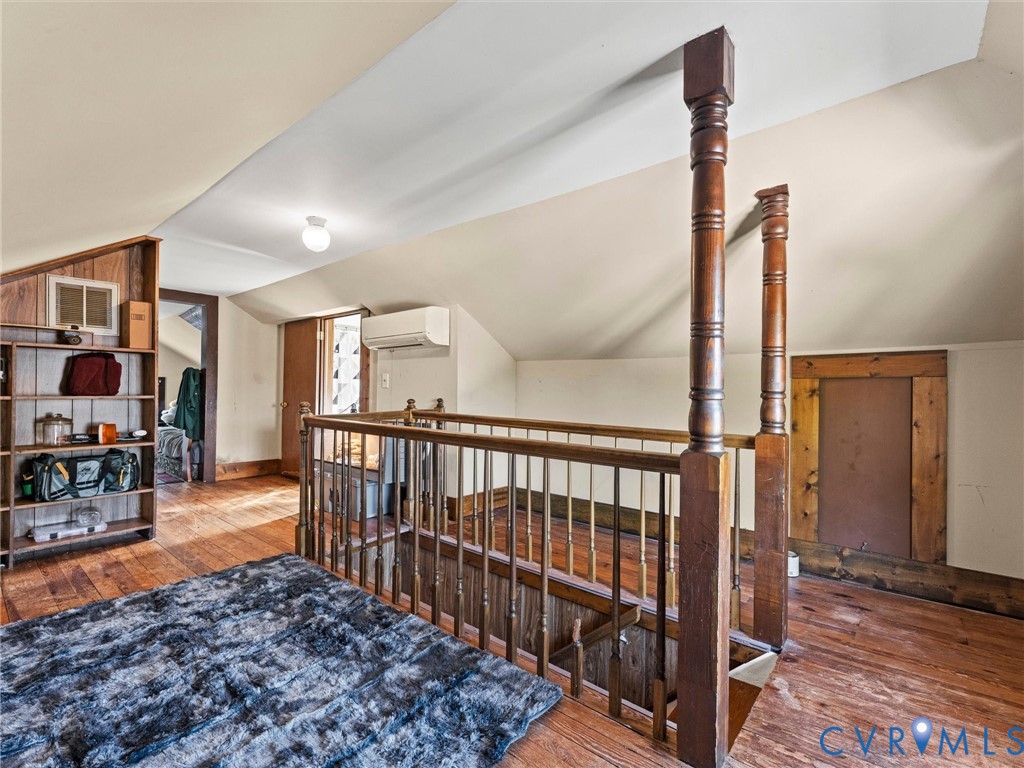 Vaulted ceiling with hardwood flooring, built-in wooden shelving, and ornate wooden stair railing
