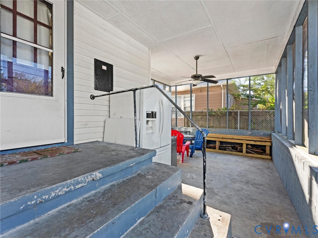 Screened-in porch featuring concrete flooring, painted masonry walls, built-in wooden shelving, and a ceiling-mounted fan