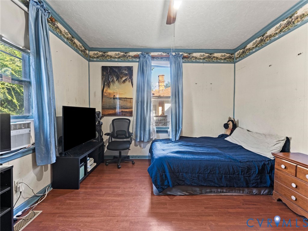 Bedroom featuring wood-finish flooring, ceiling-mounted fan/light fixture, and dual windows with decorative wallpaper border