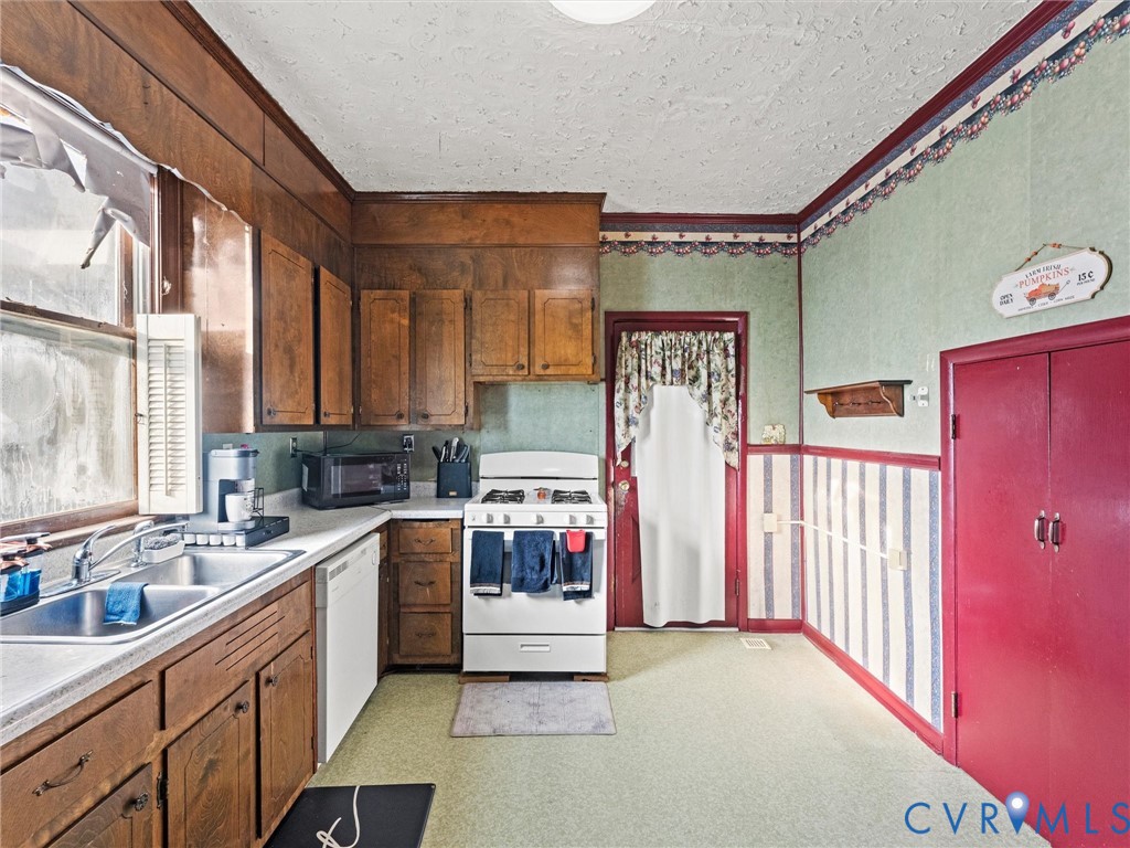 Kitchen featuring wood cabinetry, a dual-basin stainless steel sink, a freestanding range, dishwasher, and a built-in pantry closet